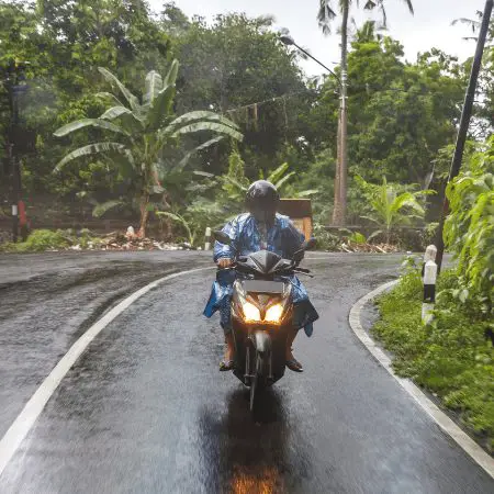 Person riding a moped on a wet road & wearing rain gear
