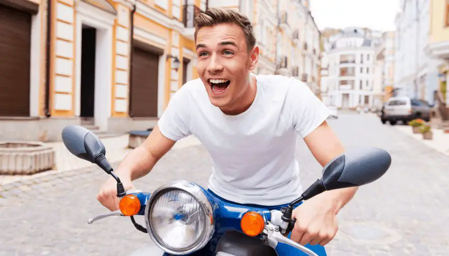 happy, young man being silly and happy sitting on a scooter in Italy