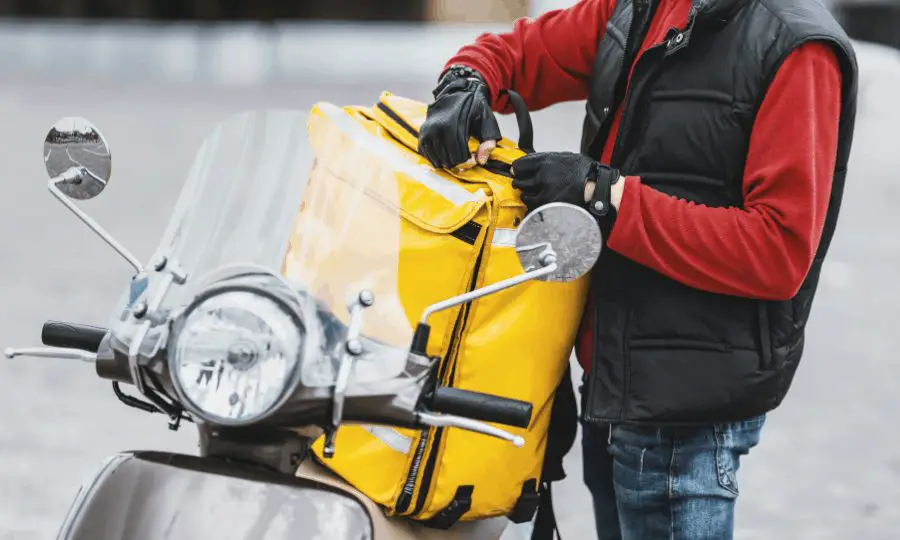 Standing Courier with Delivery Bag on Scooter Delivering Restaurant Food