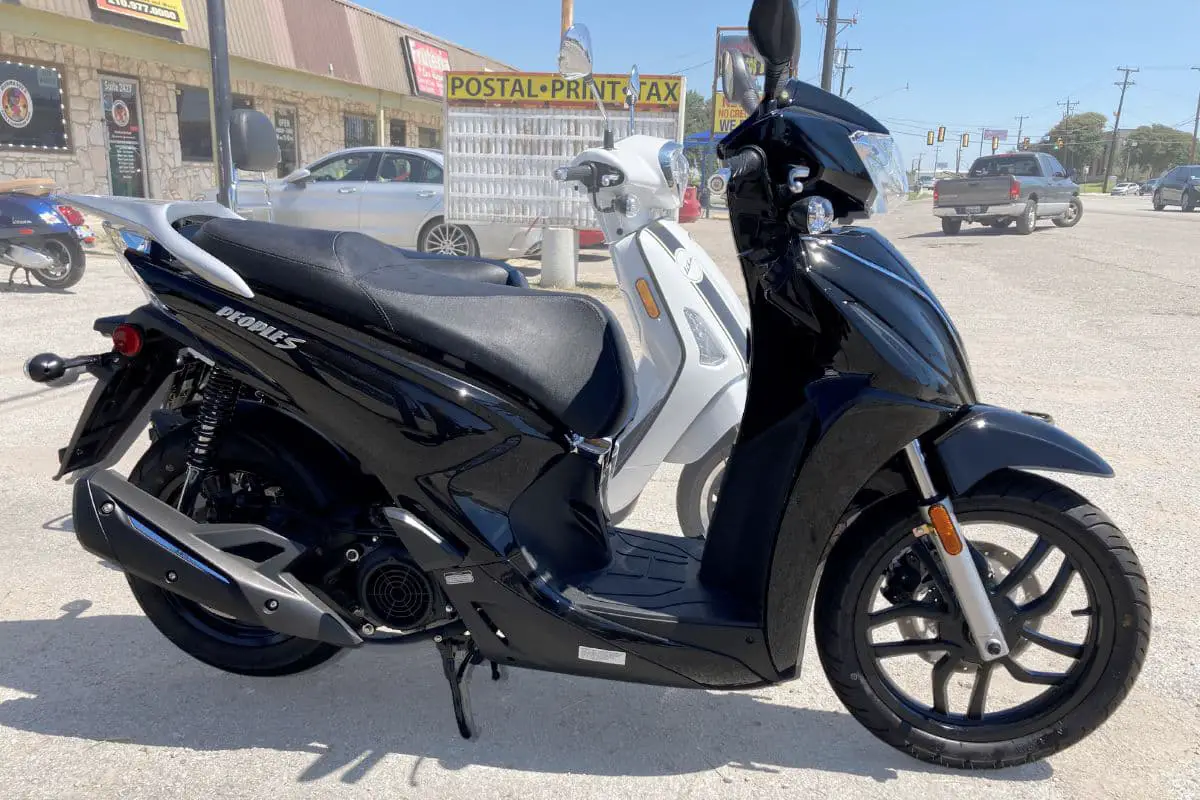 black Kymco People at a dealer in front of a white Like model