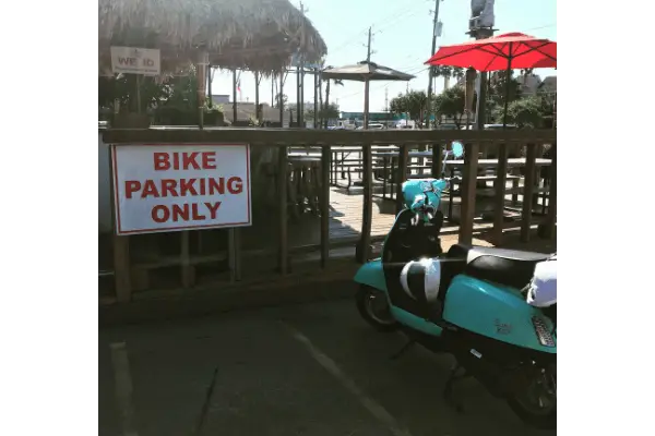 Bike parking only sign next to a scooter at an outdoor eating area