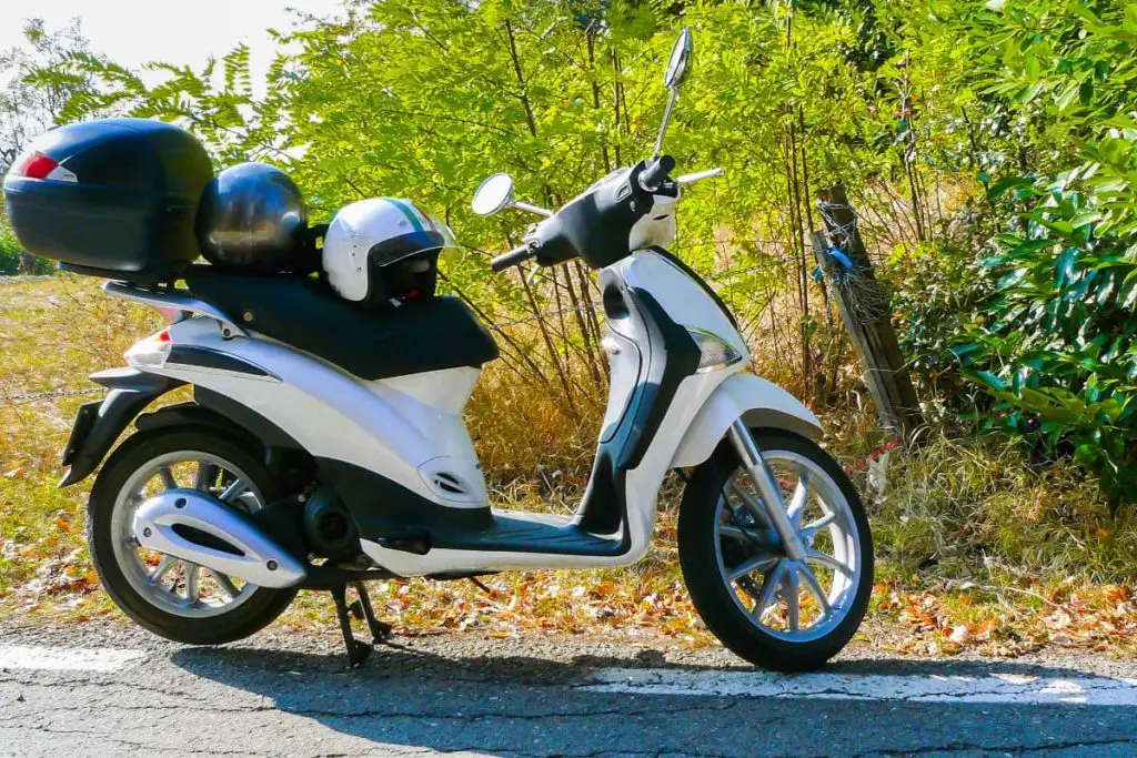 Piaggio Liberty on the side of the road with 2 motorcycle helmets balanced on the scooter seat.