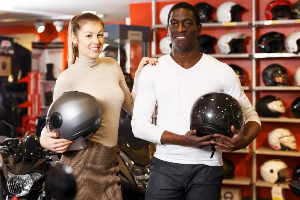 a man and woman shopping for a motorcycle helmet in a motorcycle store