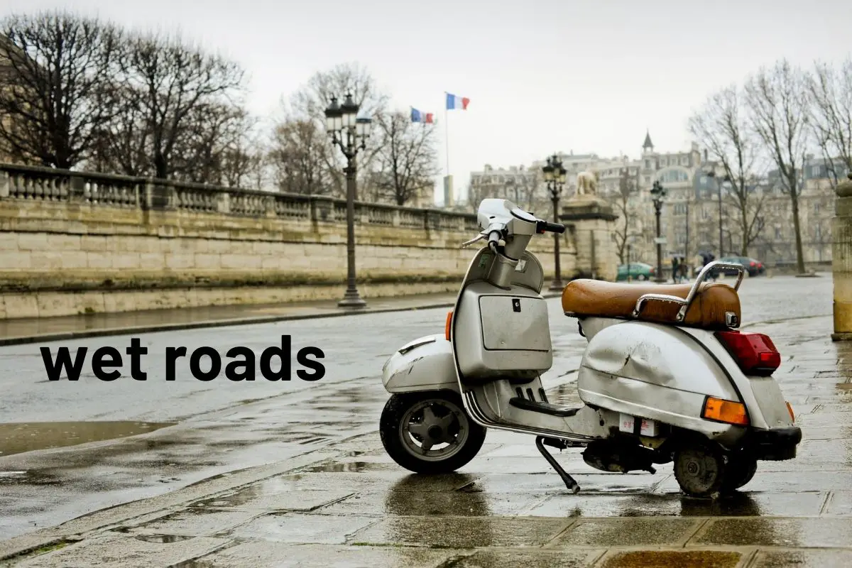 beat up vespa missing a wheel on a wet sidewalk of a wet road 