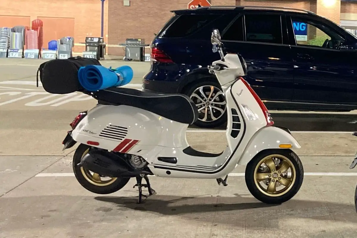 White Vespa GTS with red stripes with gold rims. Black seat has white piping and curves that make it look difficult to shave