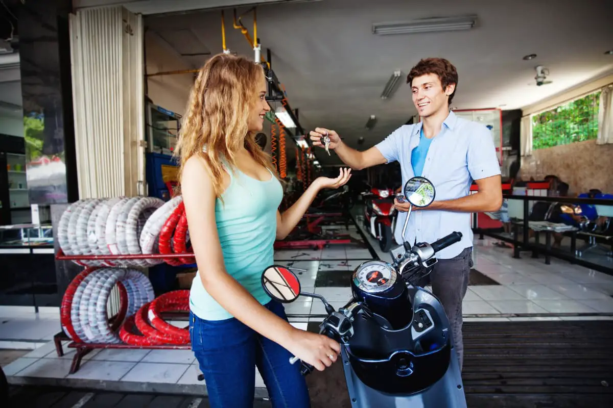 man at repair shop handing keys to scooter to woman