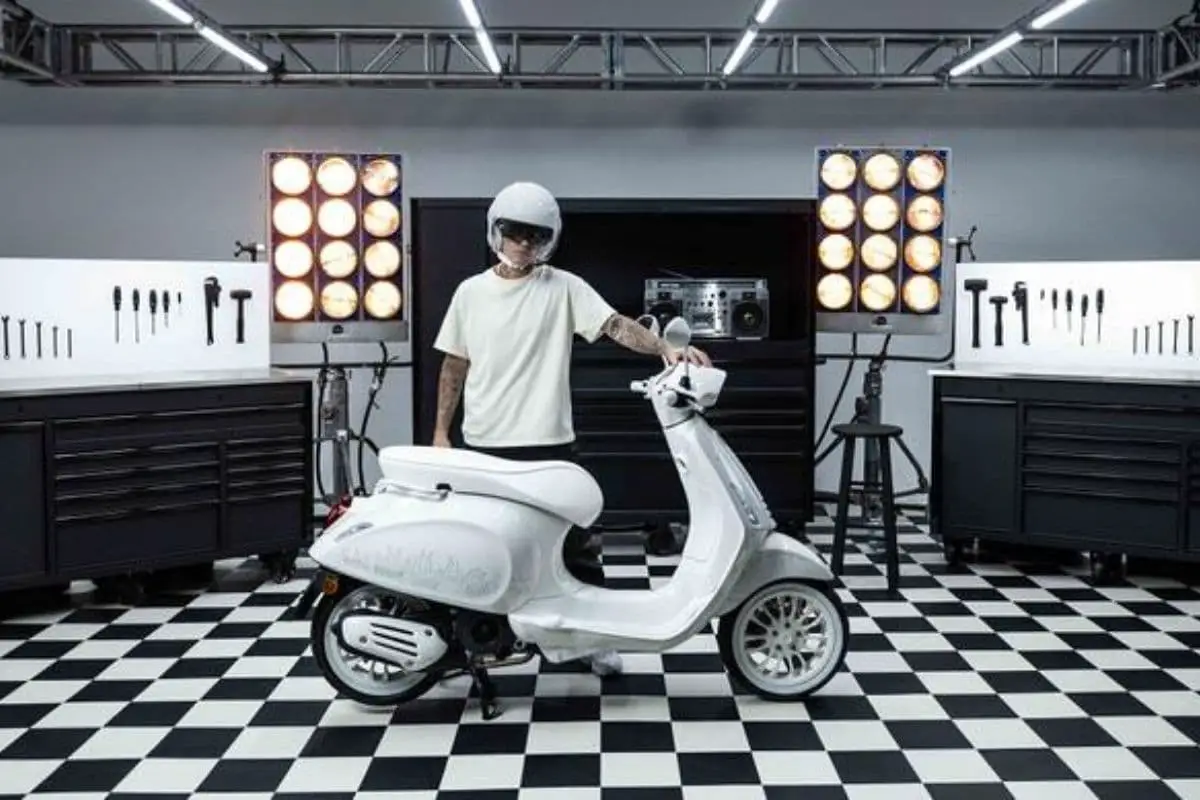 Justin Bieber standing with the result of the Vespa/Justin collaboration in a studio type garage