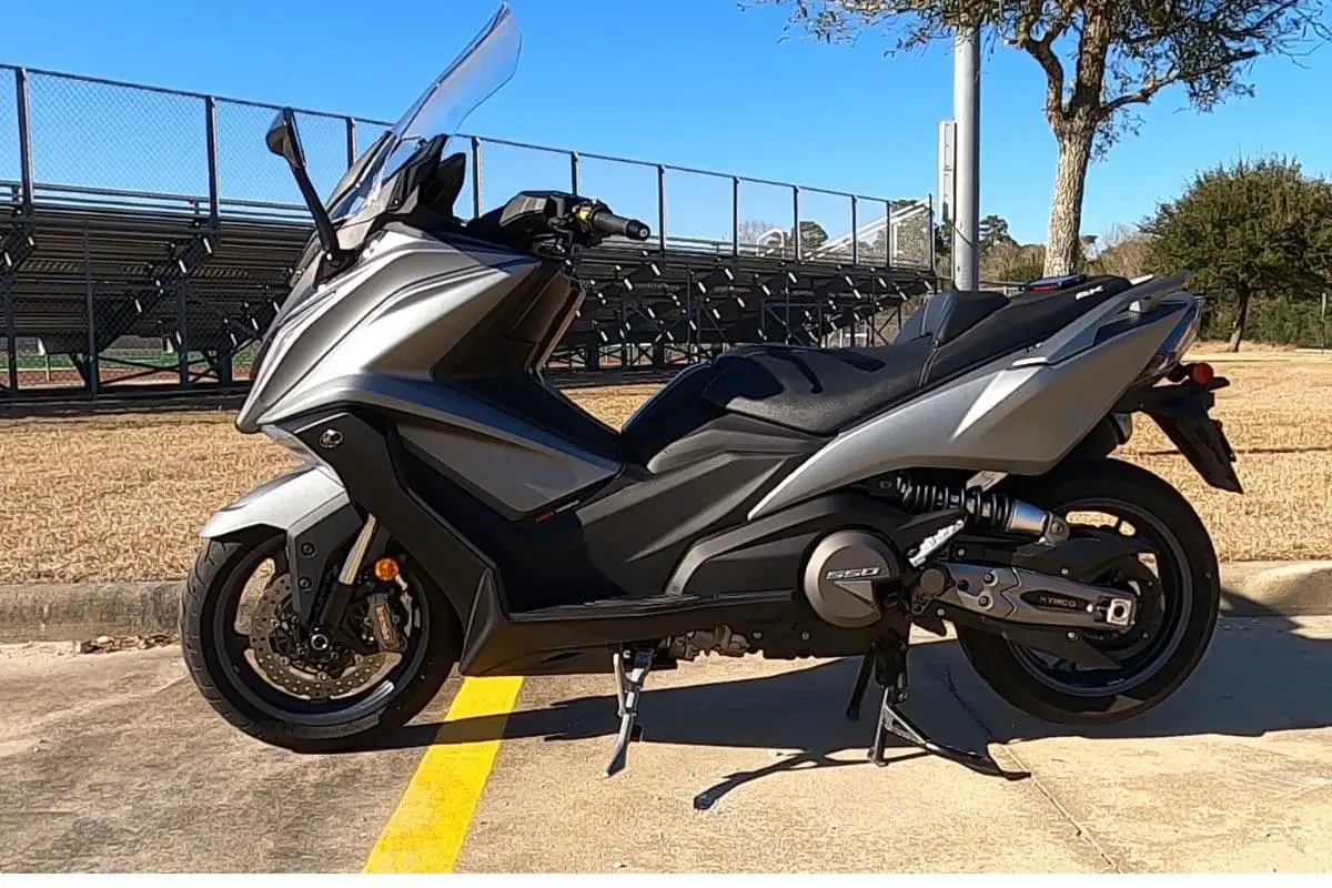 Side view of a matte silver 2022 Kymco AK550 on center stand in a parking lot