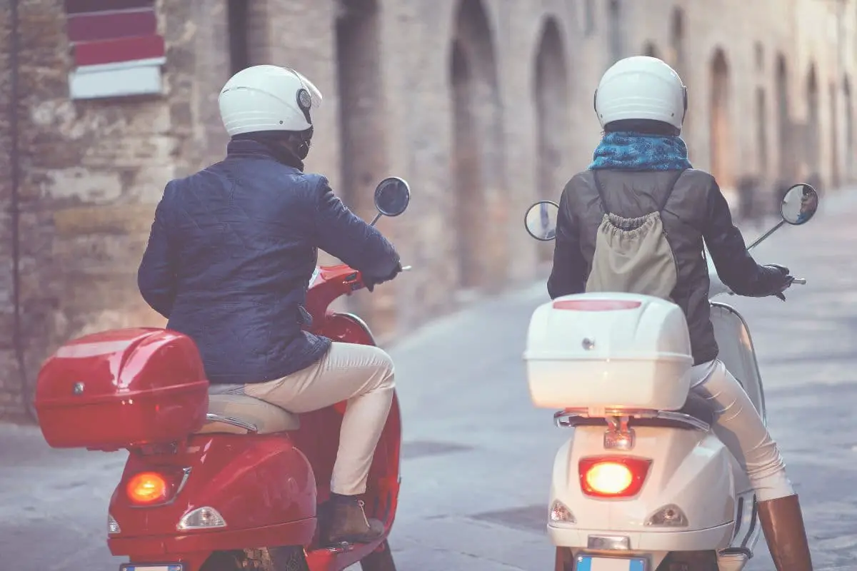 rear view of man and woman on scooters with white helmets