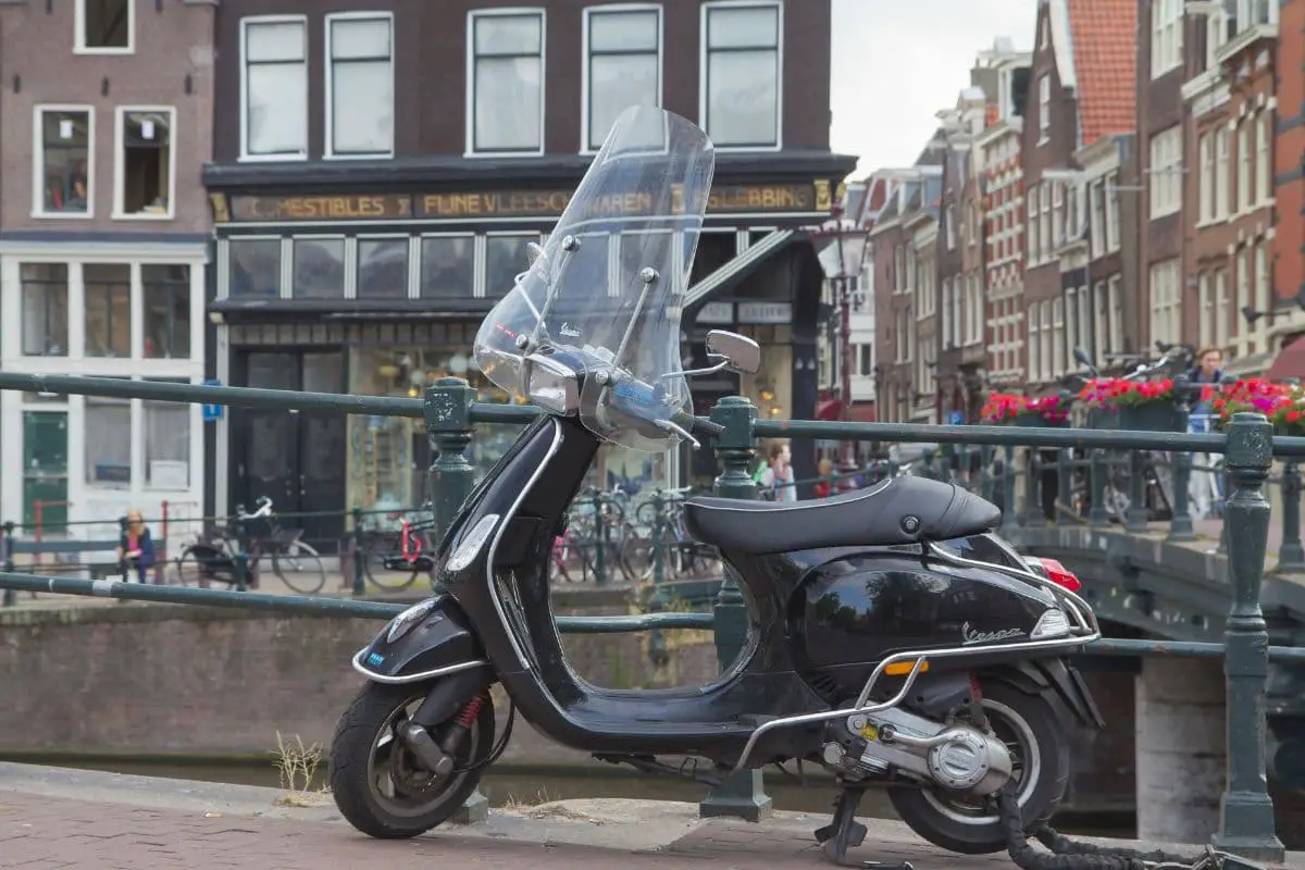 dark vespa with cowl guards and windshield on a city roadway