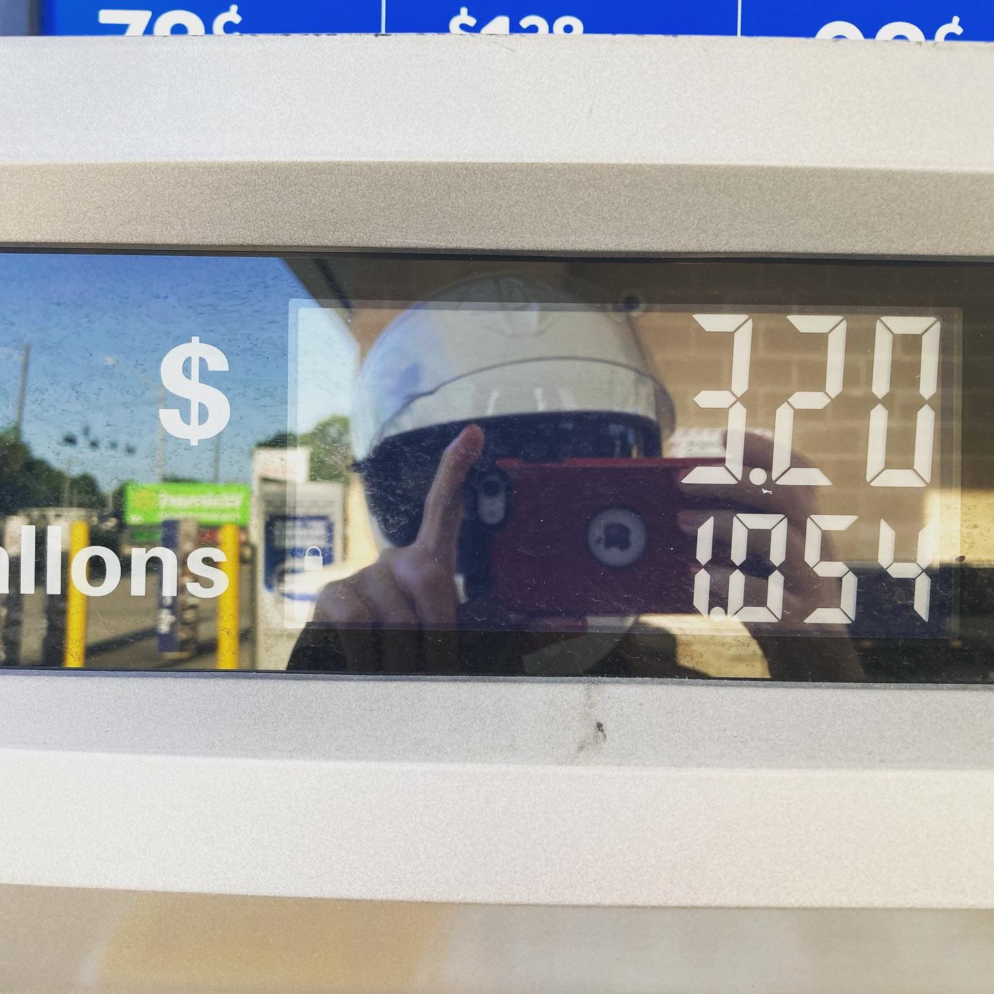 Gas pump display with 1.054 gallons that cost $3.20 with reflection of phone and helmet in the background