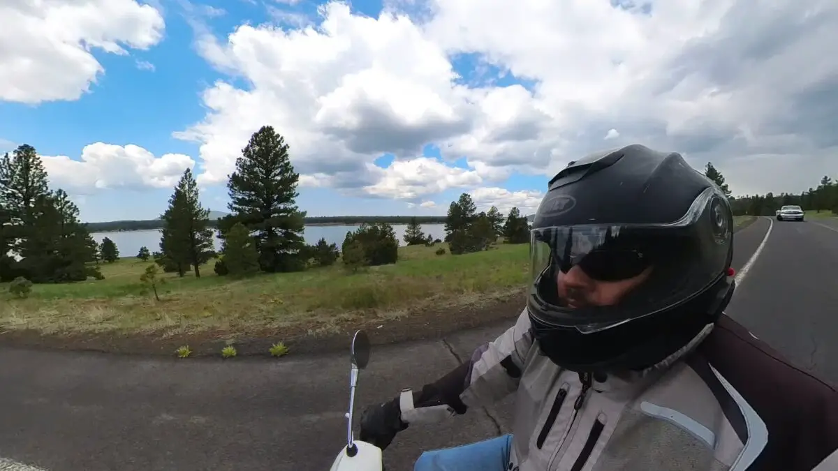 man riding a scooter next to a body of water with a blue sky and pretty clouds