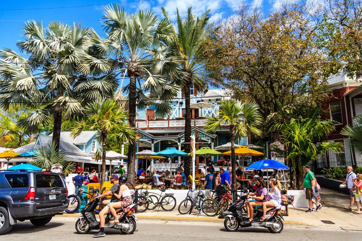 Crowded road in a beach-like town with congestion. Car, scooters, mopeds & bikes on a sidewalk