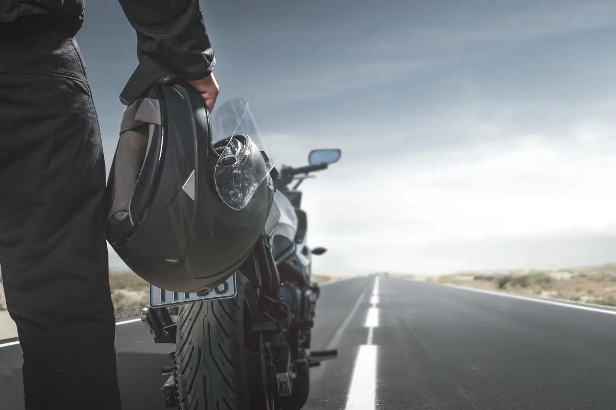 Right leg and hand of rider holding a helmet presumably looking at the open road by his motorcycle